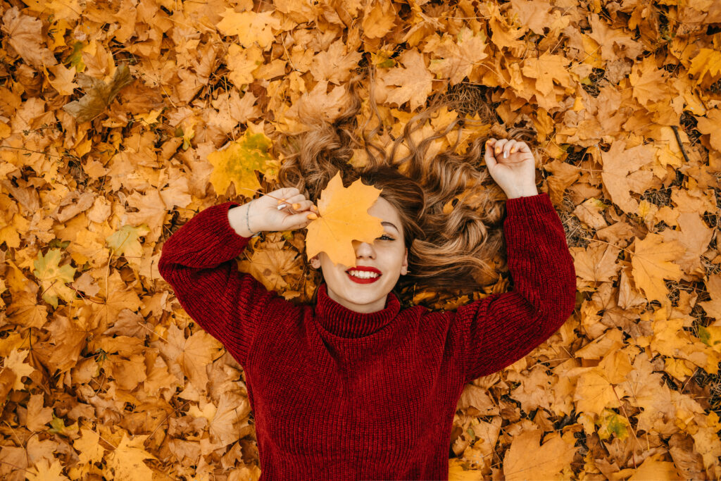 Mujer sonriendo entre hojas de otoño, una estación donde muchas personas notan una mayor caída estacional del cabello por el cambio de fase capilar.